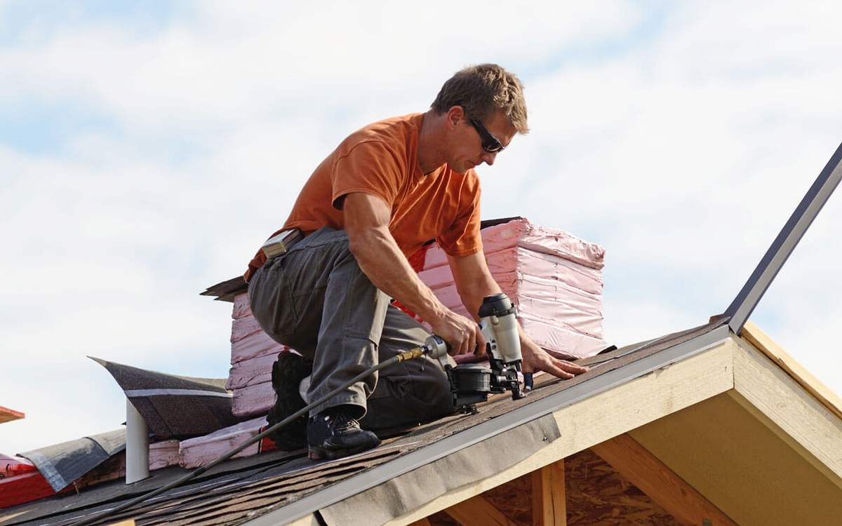 Roofer working along a roof edge replacing storm-damaged shingles